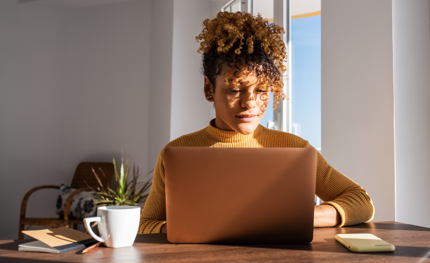 A woman in a tan turtleneck sweater working on a laptop.png